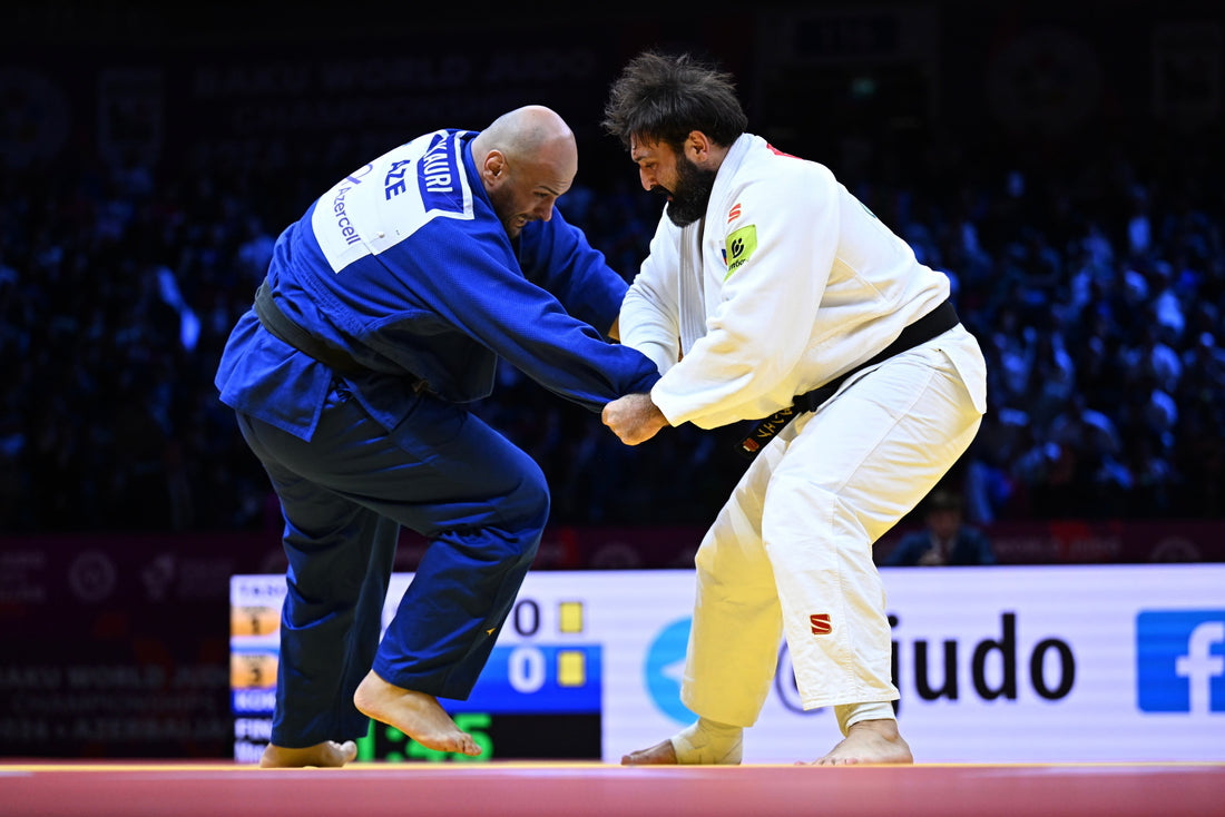 A judoka in a blue judogi and a judoka in a white judogi grip each other on a competition mat.